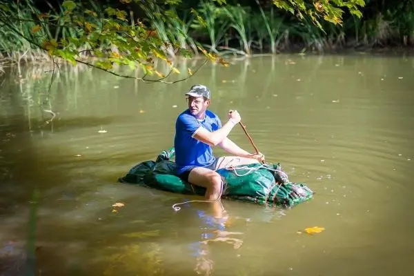 Person paddelt auf einem selbstgebauten Floß im Wasser