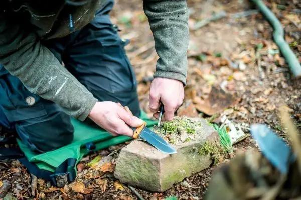 Person schneidet mit einem Messer auf einem Stein