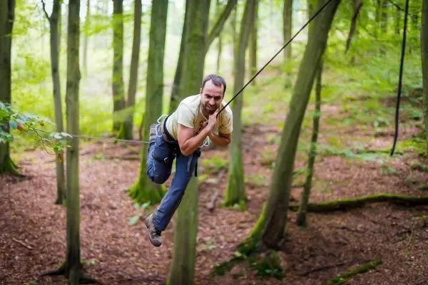 Person schwingt an einem Seil zwischen Bäumen