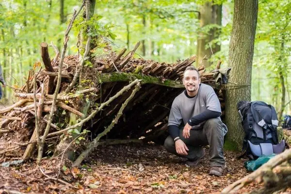 Selbstgebaute Laubhütte im Wald mit Rucksack daneben