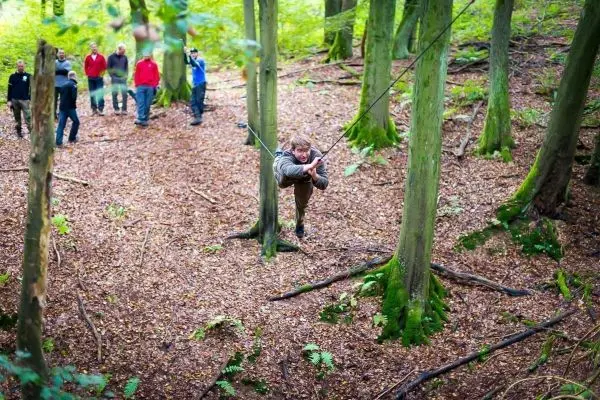 Teilnehmer überquert eine selbstgebaute Seilbrücke zwischen zwei Bäumen