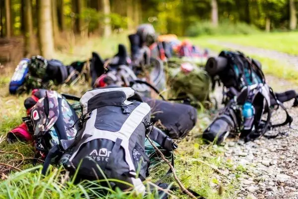 Zahlreiche Rucksäcke liegen auf einem Waldweg im Gras