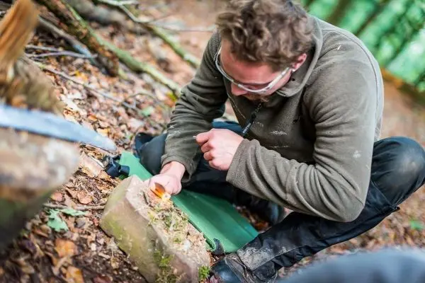Zunder glimmt auf einem Holzstück während jemand mit einem Messer arbeitet