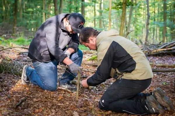 Zwei Personen arbeiten gemeinsam an einer Holzstruktur im Wald