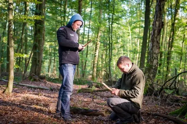 Zwei Personen bearbeiten Holzstücke im Wald
