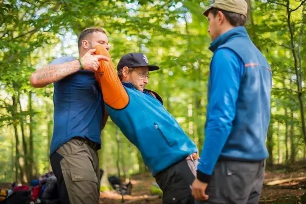 Zwei Personen demonstrieren eine Technik mit einem orangefarbenen Hilfsmittel im Wald