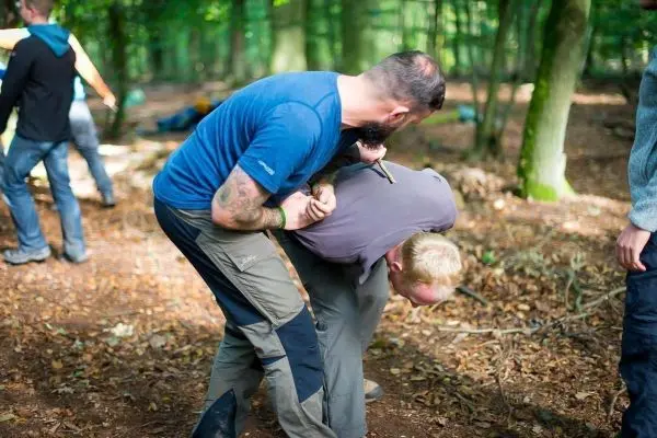 Zwei Personen in einem Wald, eine Person hält die andere in einer kontrollierten Position