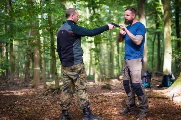 Zwei Personen in Waldumgebung führen eine Interaktion mit einer Waffe durch