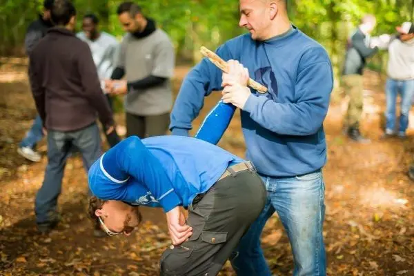 Zwei Personen üben eine Selbstverteidigungstechnik im Wald mit einem Stock
