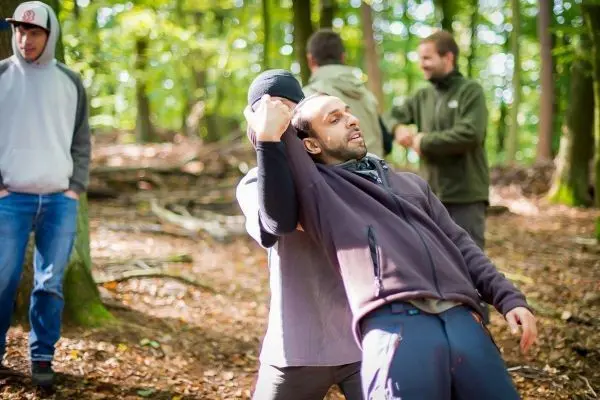 Zwei Personen üben eine Technik im Wald, während andere im Hintergrund beobachten