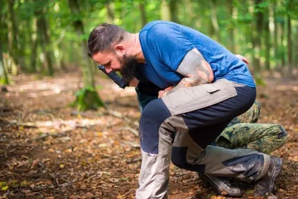 Zwei Personen unterstützen sich im Wald, eine kniet auf dem Boden