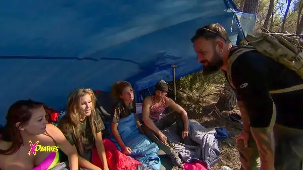 Gruppengespräch unter einem Tarp, Schlafsäcke und Ausrüstung sichtbar