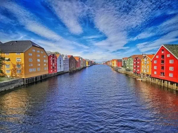 Bunte Holzhäuser stehen am Ufer eines ruhigen Gewässers unter blauem Himmel