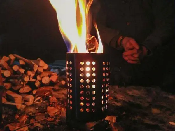 Feuer in einem Behälter mit Löchern, Holzstapel im Hintergrund