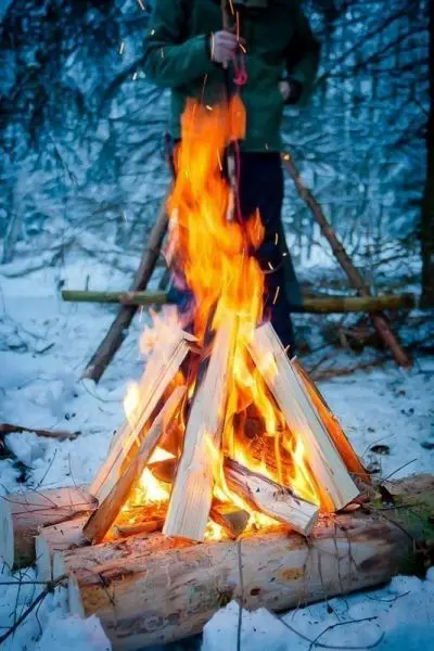 Feuerstelle mit brennendem Holz im Schnee, Person im Hintergrund