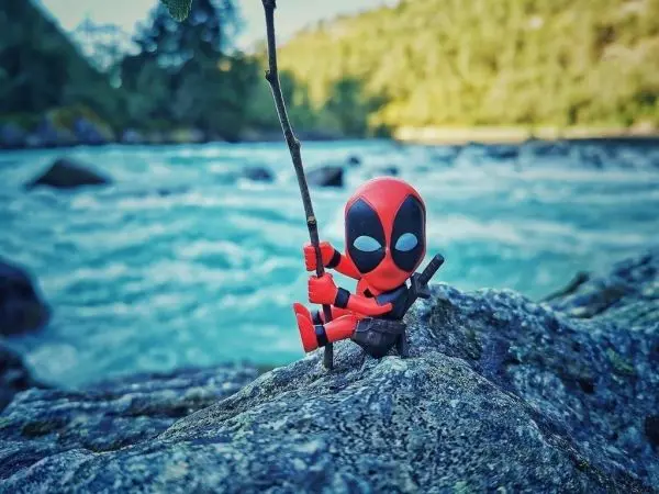 Figur mit rotem und schwarzem Kostüm sitzt auf einem Stein am Wasser