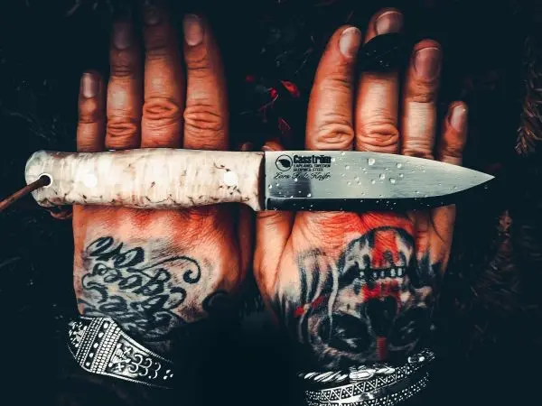 Hände mit Tätowierungen halten ein Messer mit hellem Griff
