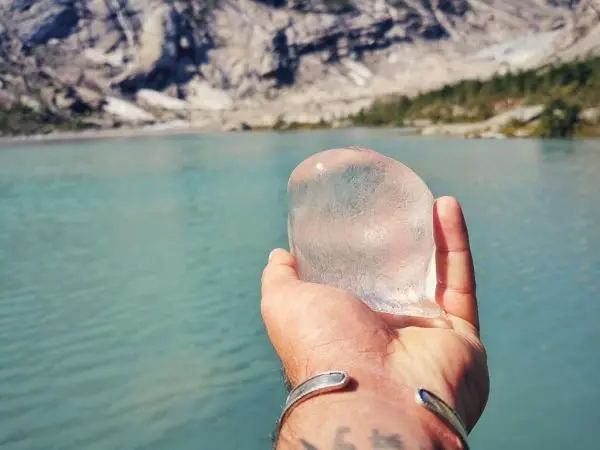 Hand hält ein großes Stück Eis über einem klaren Gewässer