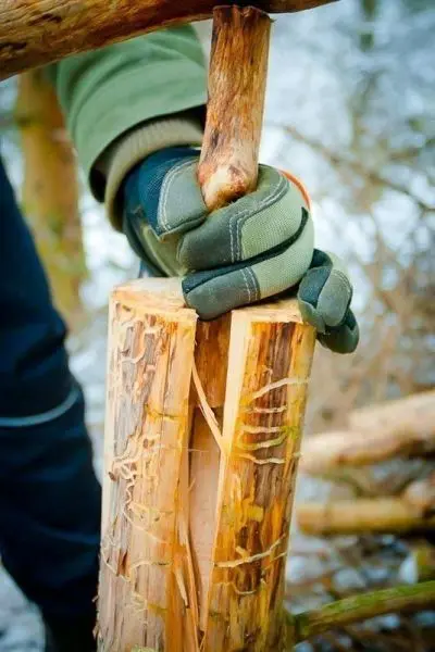 Hand mit Handschuh hält einen Stock über einem gespaltenen Holzstück