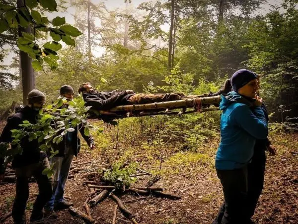 Improvisierte Trage wird von mehreren Personen durch den Wald getragen