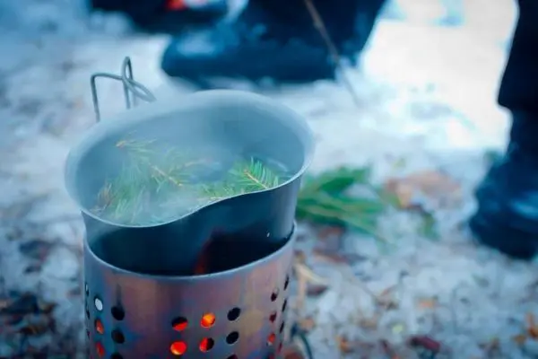 Kessel mit Zweigen dampft über Hobo-Kocher auf schneebedecktem Boden
