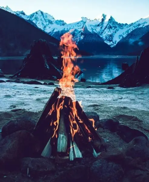 Kleine Flamme brennt zwischen Holzscheiten am Ufer eines Sees