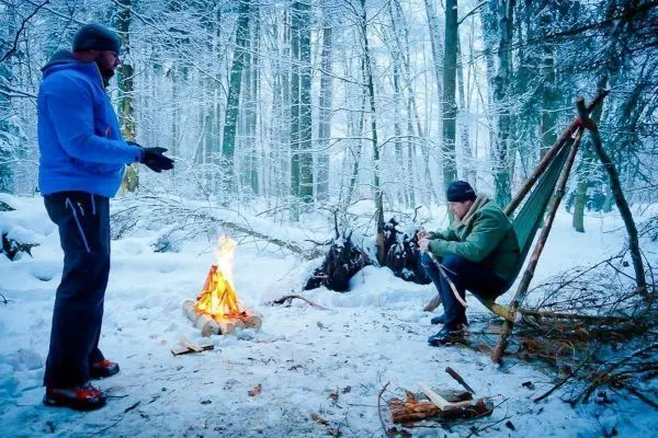 Kleines Bodenfeuer wärmt in verschneiter Umgebung, während eine Person an einem improvisierten Sitz arbeitet