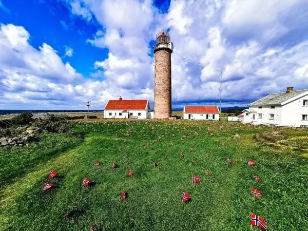 Leuchtturm steht neben weißen Gebäuden auf grünem Rasen mit kleinen Flaggen