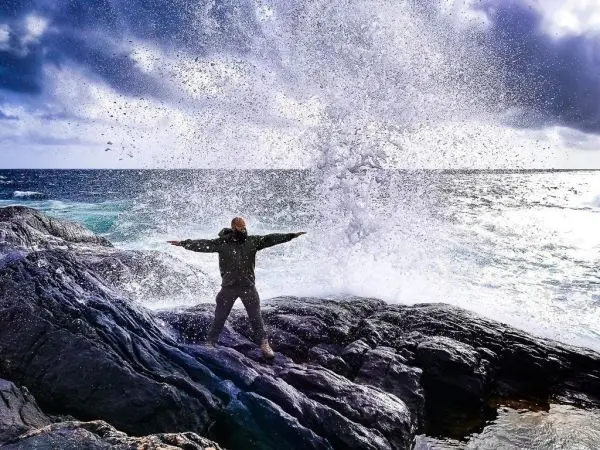 Mann steht auf Felsen und wird von Wasserfontäne umgeben