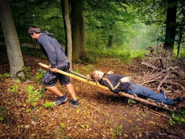 Mann zieht improvisierte Trage mit einer Person durch den Wald