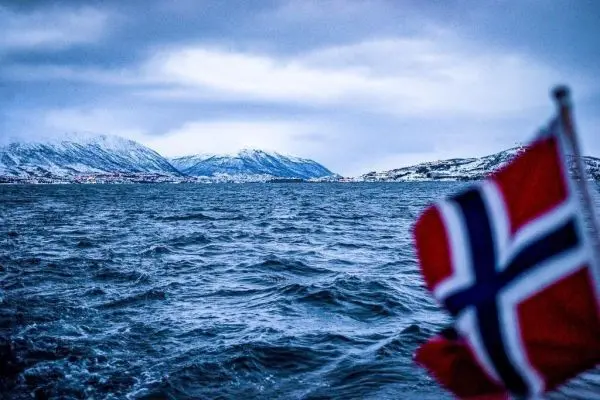 Norwegische Flagge im Vordergrund, Berge und Wasser im Hintergrund