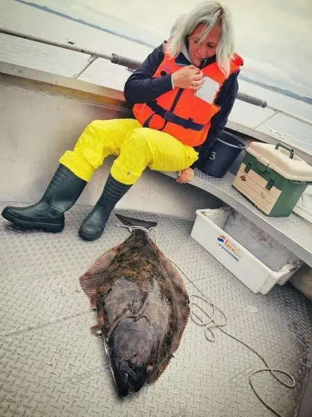 Person in orange Schwimmweste sitzt neben einem großen Fisch auf einem Boot