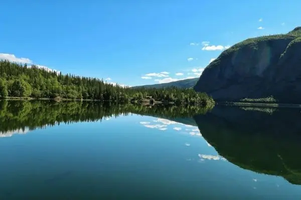 Spiegelnde Wasseroberfläche mit umliegenden Bäumen und Bergen im Hintergrund