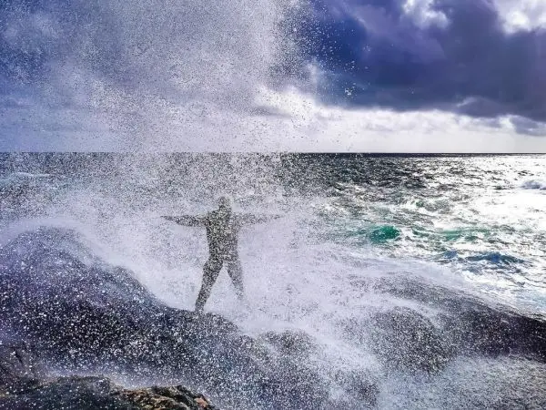 Spritzendes Wasser schlägt gegen Felsen, während eine Person mit ausgebreiteten Armen steht
