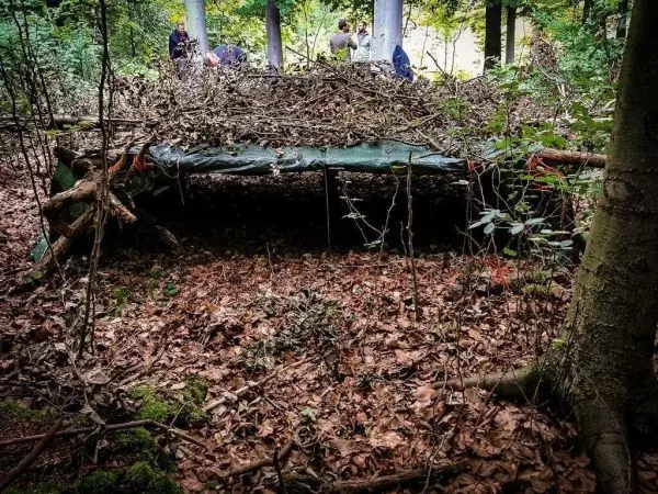 Tarp-Notunterkunft aus Ästen und Laub im Wald aufgebaut