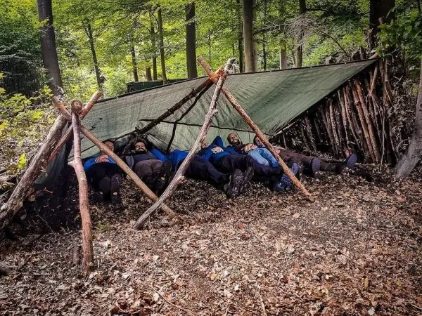 Tarp-Notunterkunft aus Ästen und Plane bietet Schutz für mehrere Personen