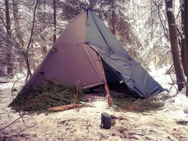 Tarp-Notunterkunft aus Plane und Ästen im Schnee, daneben ein Kochtopf