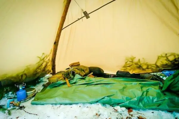 Tarp-Notunterkunft mit Schlafsack und Ausrüstung auf Schnee
