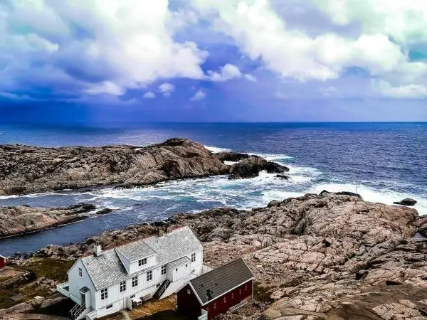 Weißes Haus und rotes Gebäude auf felsiger Küste mit Meer im Hintergrund