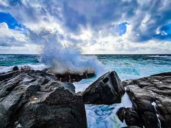 Wellen schlagen gegen große Felsen an der Küste, spritzendes Wasser in die Luft