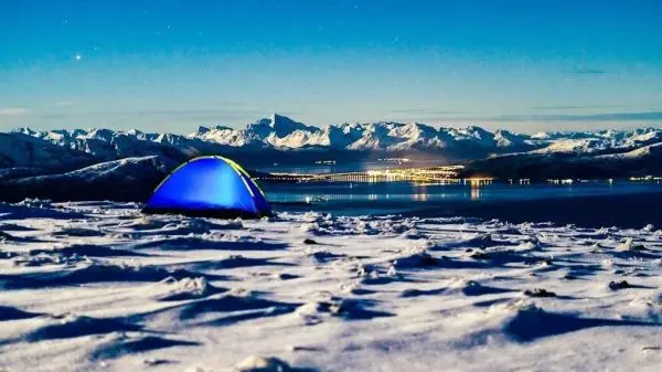Zelt auf schneebedecktem Boden mit Berglandschaft und Wasser im Hintergrund