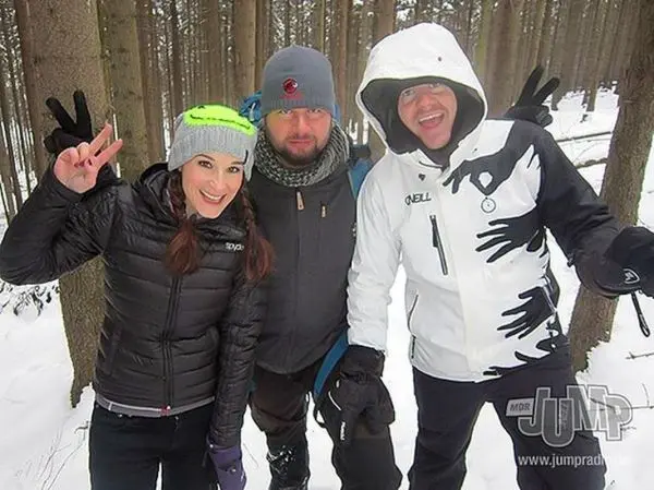 Drei Personen posieren im Schnee zwischen Bäumen, eine zeigt das Peace-Zeichen
