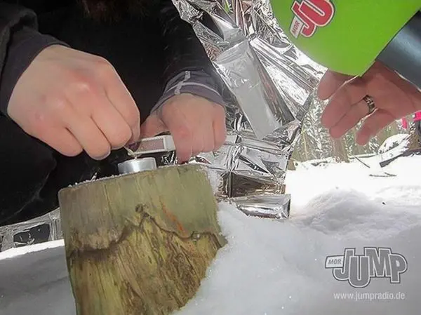 Feuerstahl erzeugt Funken auf einem Holzstück im Schnee
