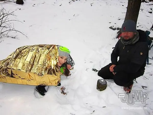 Folie-Notunterkunft schützt vor Kälte, während ein Mann neben einem Kocher sitzt
