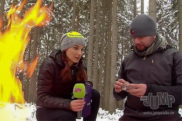 Kleine Flamme brennt neben zwei Personen im Wald, einer hält ein Metallbehältnis