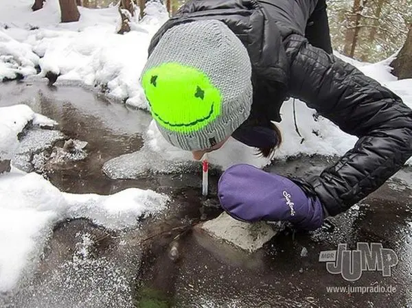 Person beugt sich über gefrorenes Wasser und nutzt einen Stift zur Messung