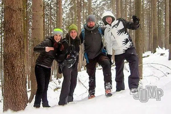 Vier Personen posieren im Schnee zwischen Bäumen, lächeln und zeigen mit den Händen