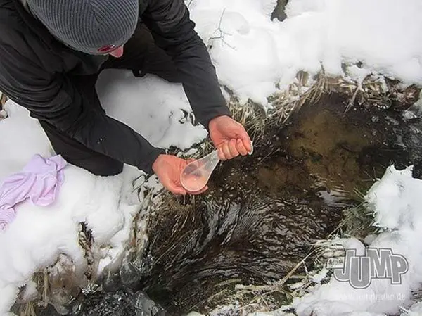 Wasser wird mit einem Behälter aus einem schneebedeckten Bach entnommen