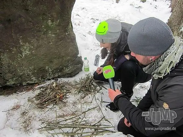 Zwei Personen bereiten Zunder aus Ästen für ein Feuer im Schnee vor