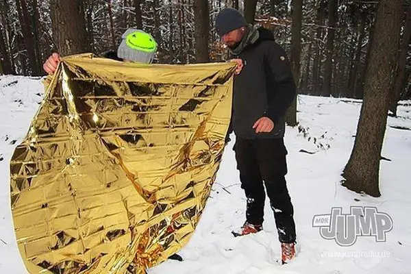 Zwei Personen halten eine reflektierende Rettungsdecke in einem verschneiten Wald